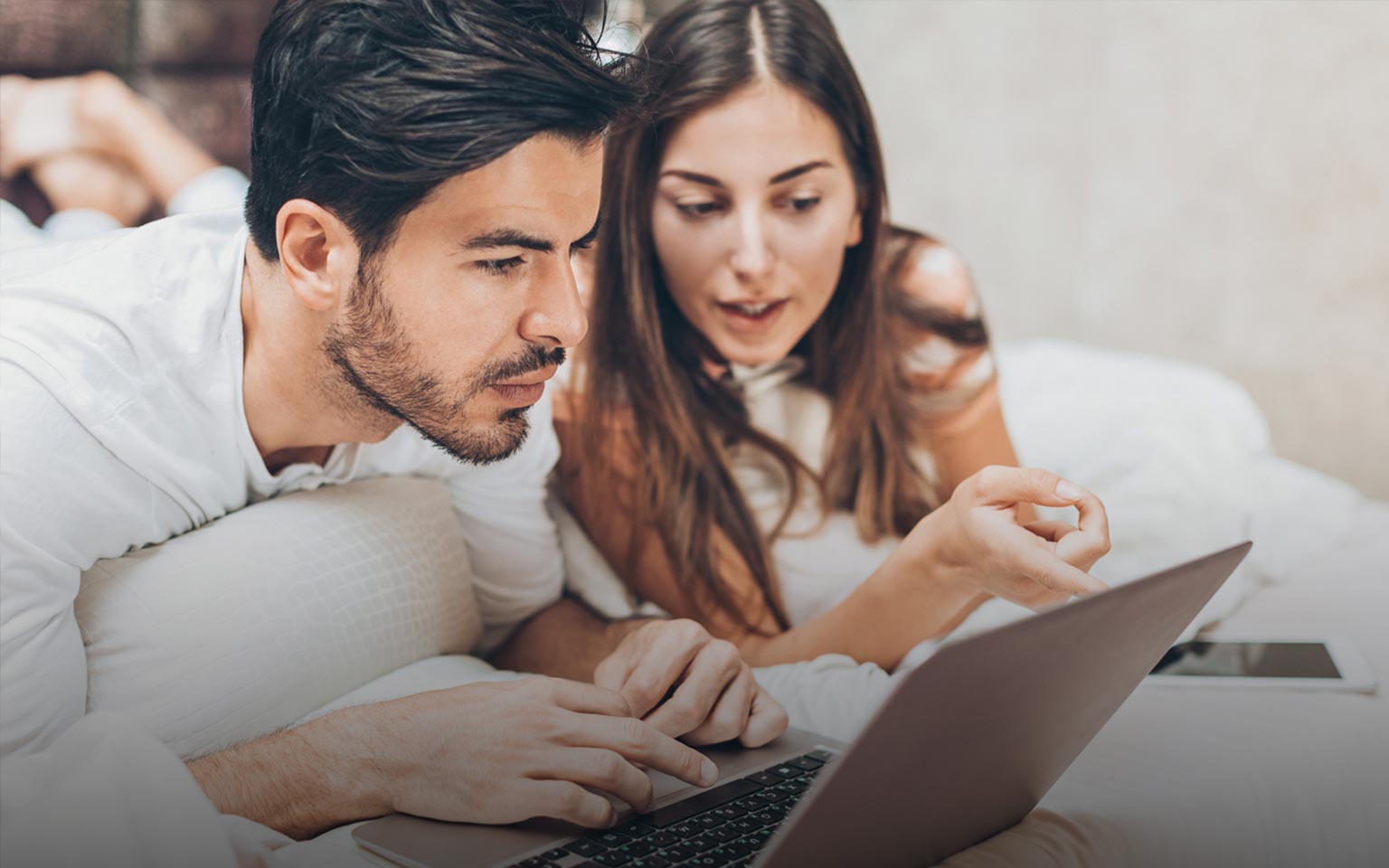 Pärchen liegt im Bett und schaut auf einen Laptop